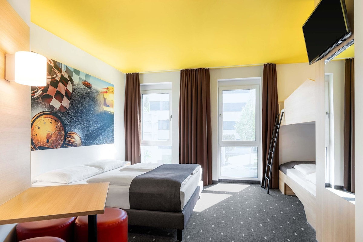 A hotel room with a bed, a desk, a chair, a TV, and a window with curtains.