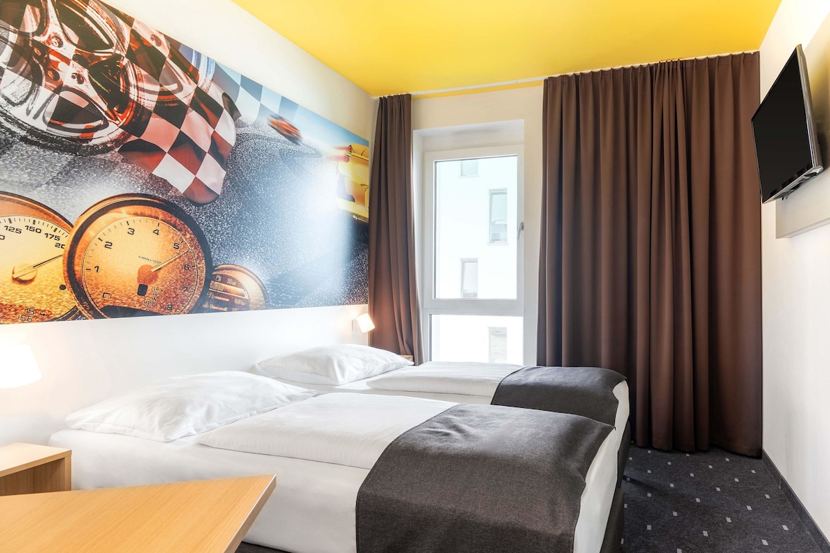 A hotel room with a bed, a desk, a TV, and a mural of clocks.