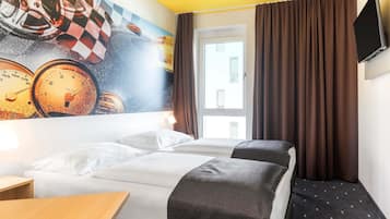 Hotellihuone, jossa on sänky, työpöytä, televisio ja seinämaalaus, jossa on kuvattuna kelloja.
