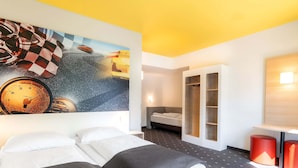 A modern hotel room with a large bed, a small sofa, a wardrobe, and a painting on the wall.