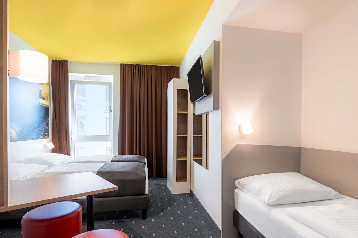 A hotel room with two beds, a desk, a chair, and a TV.
