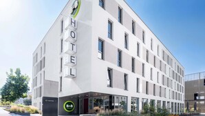 A modern hotel building with a prominent 'HOTEL' sign on the facade, a B&B logo, and a clear sky in the background.
