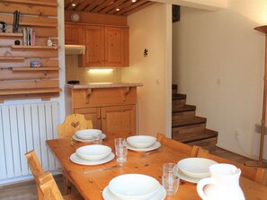 A dining area with a wooden table set for four, a kitchen with wooden cabinets, and a staircase leading to another level. - Cozy Duplex Ski Apartment, 6 Guests, Ideal Location in Vars Les Claux (Vars)
