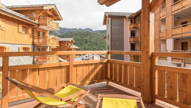 A wooden balcony with two yellow chairs, overlooking a mountainous landscape and traditional chalet-style buildings. - Ski-In/Ski-Out Apartment, 6 Guests, Terrace & Private Ensuite (Montgenèvre)