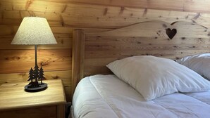 A wooden headboard with a heart-shaped cutout, a bedside lamp, and a small wooden nightstand with a tree decoration. - Ski-In/Ski-Out Apartment, 6 Guests, Terrace & Private Ensuite (Montgenèvre)