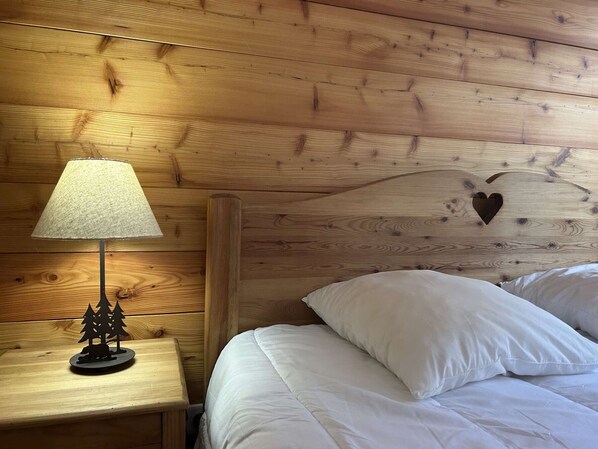 A wooden headboard with a heart-shaped cutout, a bedside lamp, and a small wooden nightstand with a tree decoration.