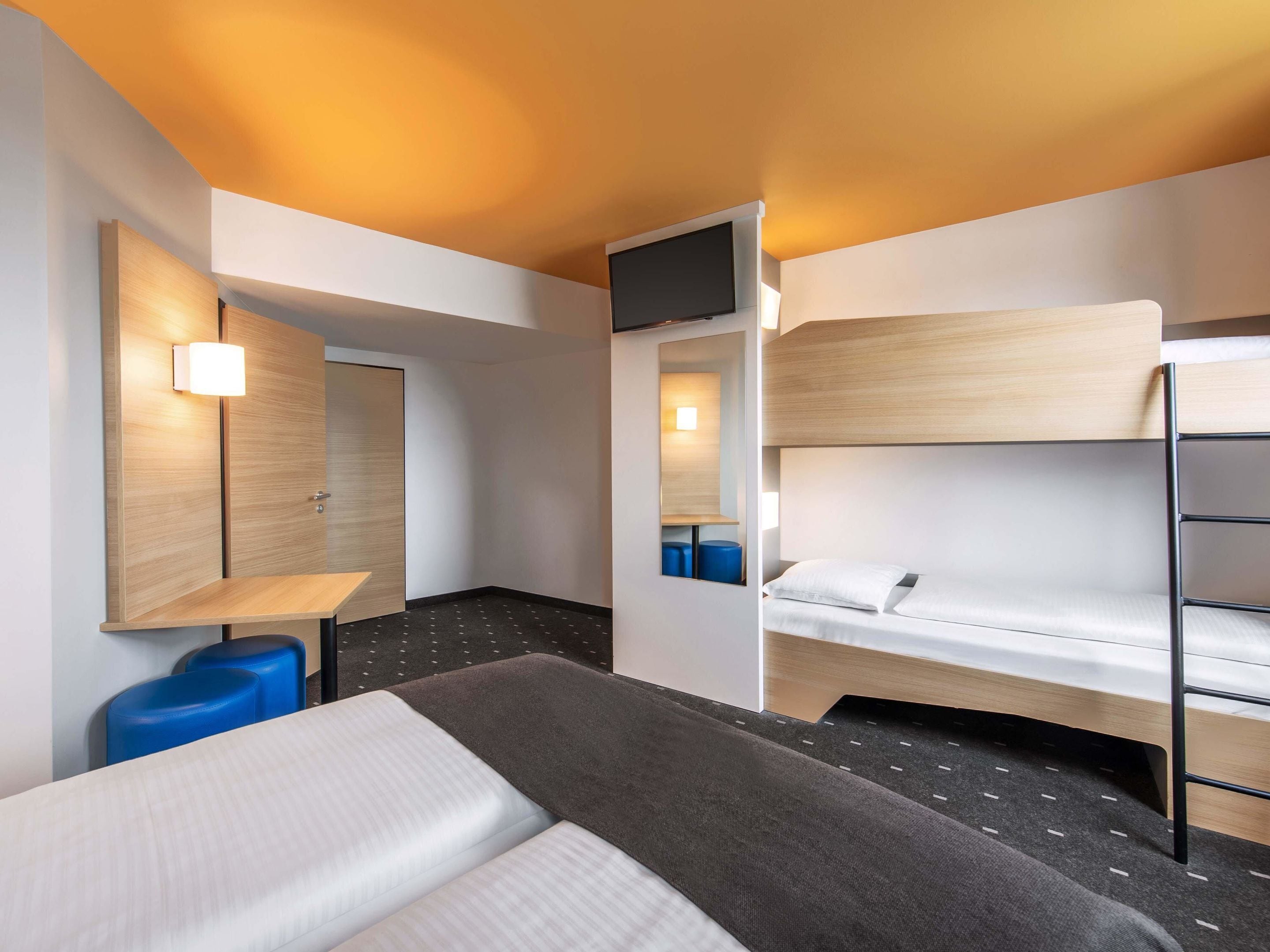 Ein Hotelzimmer mit Etagenbett, Schreibtisch mit Stuhl, Fernseher und Spiegel.