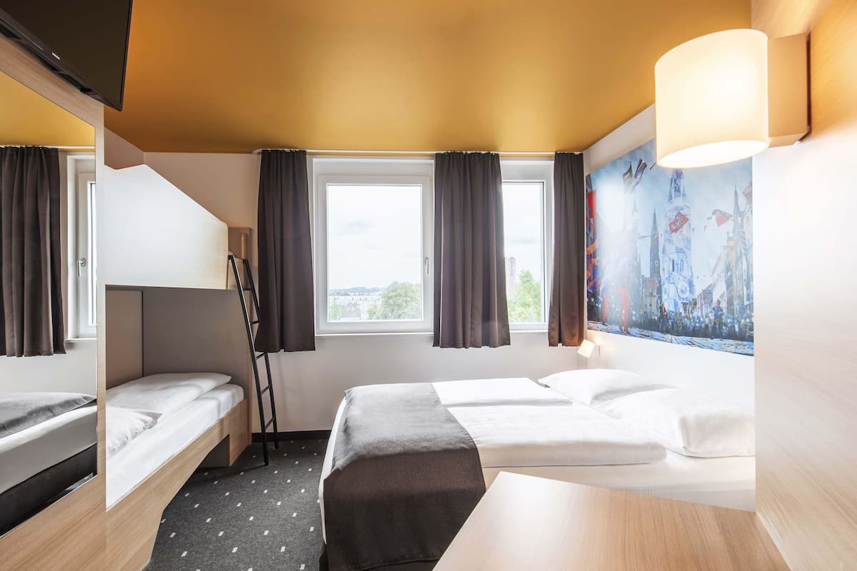 A hotel room with bunk beds, a desk, a chair, a ladder, and a large window with curtains.