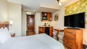 A hotel room with a large bed, a television, a wooden dresser, a desk, and a kitchenette.