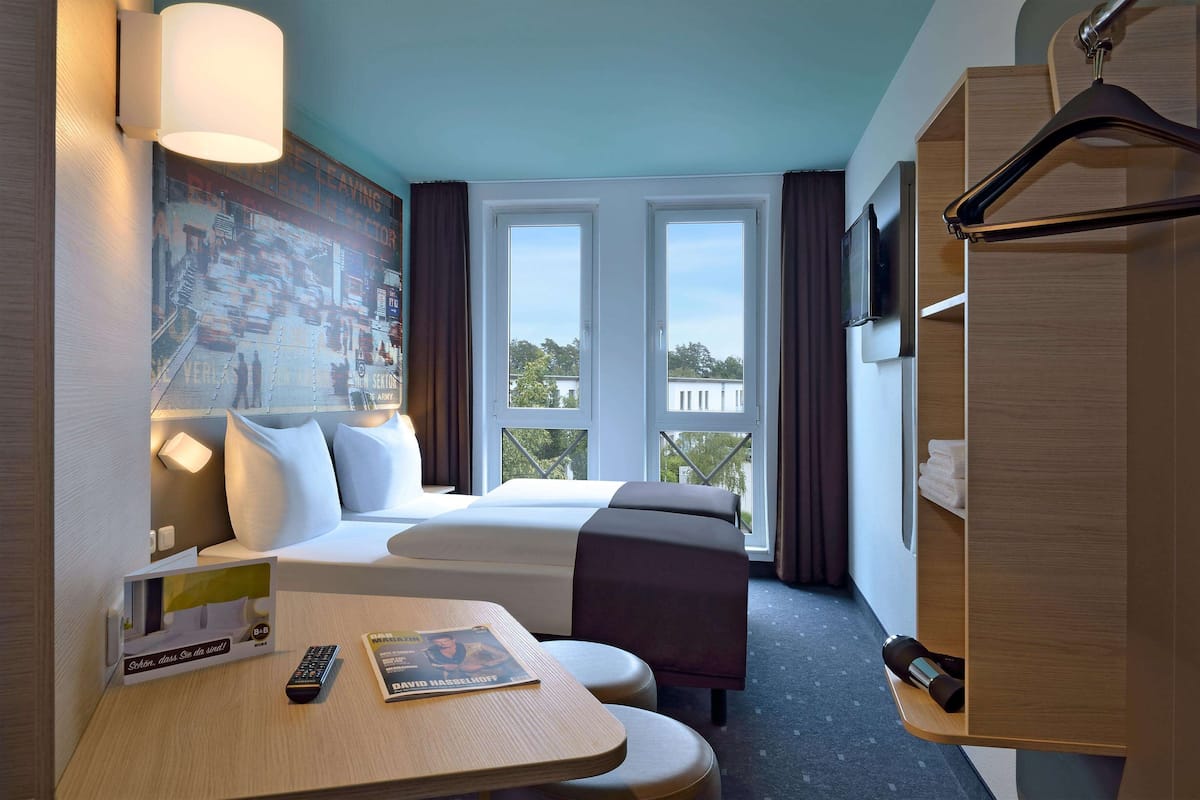 A hotel room with a bed, a desk, a TV, and a large window with curtains.