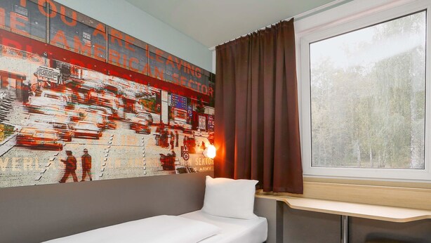 Une chambre d’hôtel avec un lit, un bureau, une fenêtre avec des rideaux et un mur orné d’une fresque.