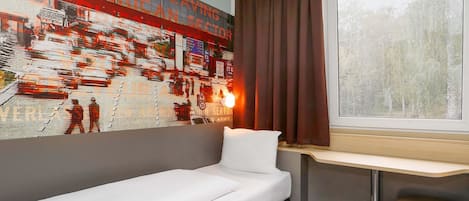 Habitación de hotel con cama, escritorio, ventana con cortinas y un mural en la pared.
