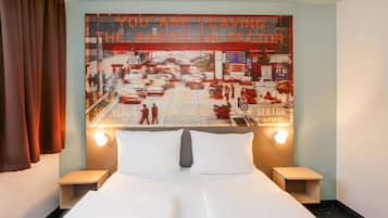A hotel room with a bed, two bedside tables, and a large wall mural depicting a city street scene with a message about leaving the American sector.