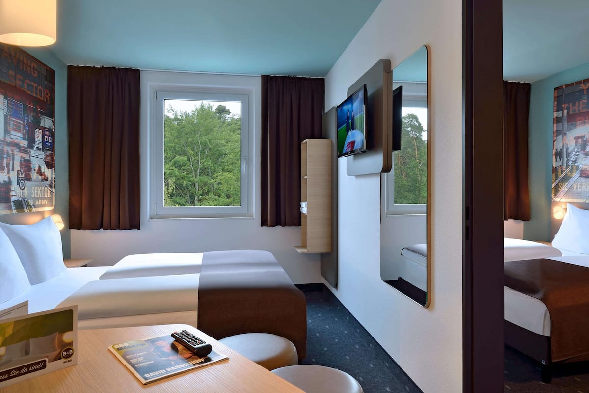 A hotel room with two beds, a TV, a desk with a remote, and a window with curtains.