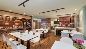 Een modern café met witte tafels en stoelen, een koffiebar met diverse dranken, en een stadsgezicht door het raam.