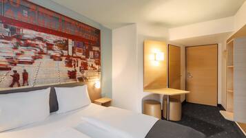 Une chambre d’hôtel avec un grand lit, une table de chevet, une lampe fixée au mur, une petite table et une porte.