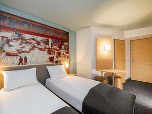 Een hotelkamer met twee bedden, een groot abstract schilderij aan de muur, een nachtkastje met een lamp en een houten deur.