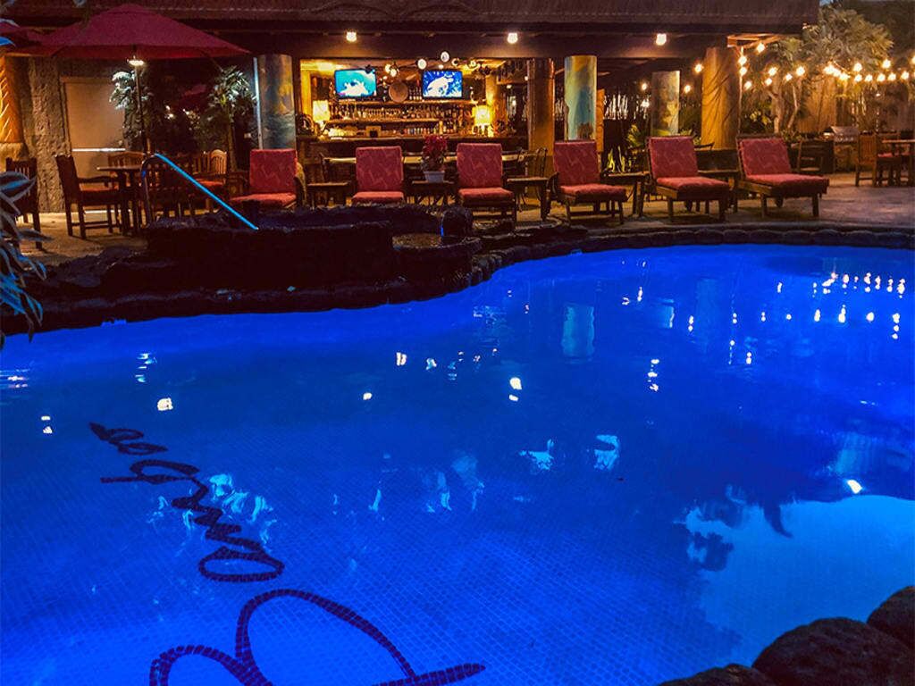 Una piscina con zona de bar y sillas rojas al fondo.