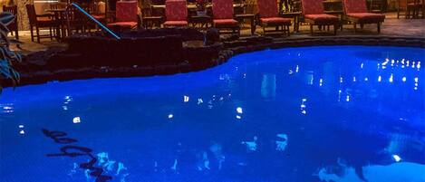 Una piscina con zona de bar y sillas rojas al fondo.