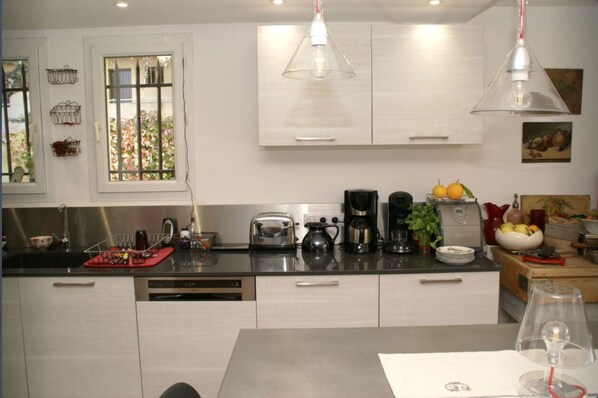 A modern kitchen with white cabinets, stainless steel appliances, and a window with a view of greenery.