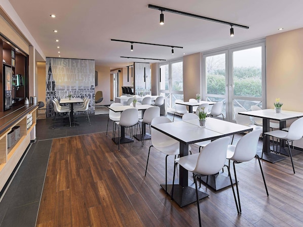 A modern dining area with multiple tables and chairs, large windows, and a wooden floor. - B&B Hotel Köln-West (Cologne)
