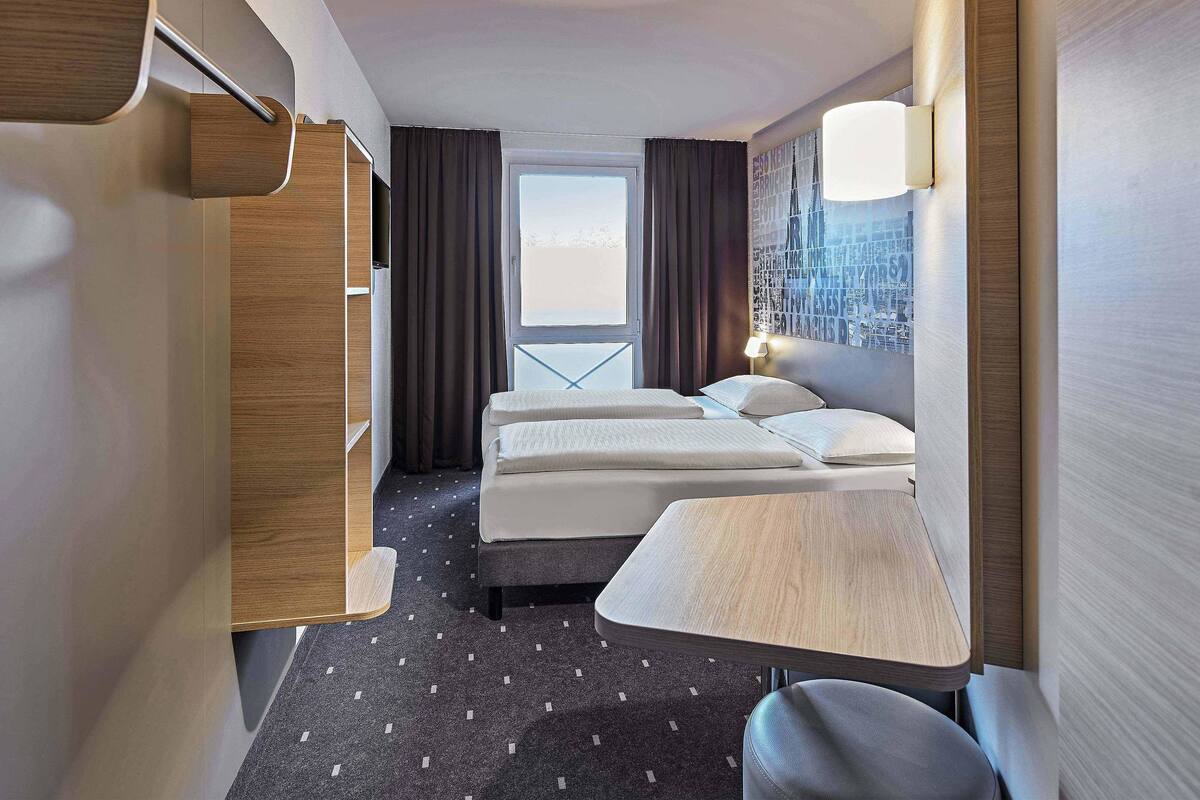 A hotel room with a bed, a desk, a chair, and a window with curtains.