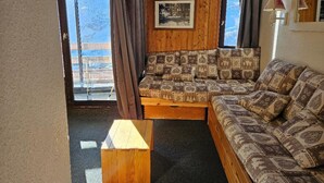 Un salon chaleureux avec un canapé et une table basse en bois, un tableau encadré au mur et une vue sur un paysage enneigé par la fenêtre.