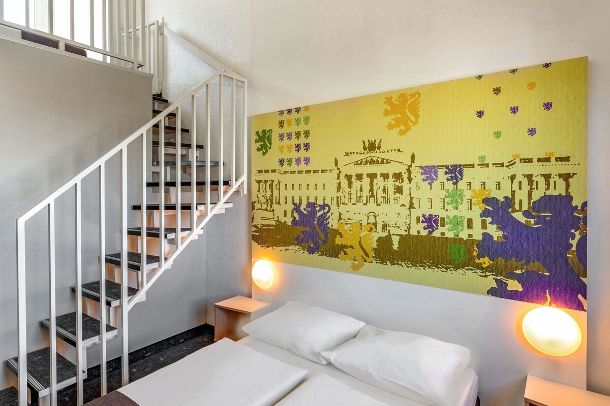 Una habitación de hotel con una cama, una escalera blanca y un mural de colores.