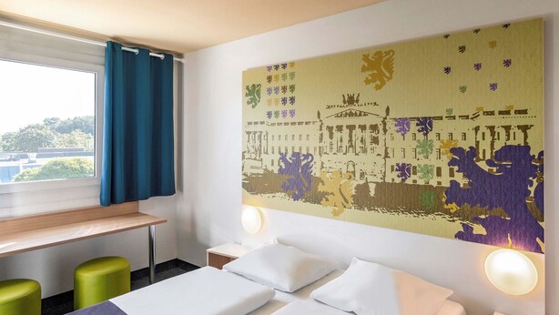 A hotel room with a bed, two green stools, a desk, and a large wall mural. - B&B Hotel Braunschweig-Nord (Braunschweig)