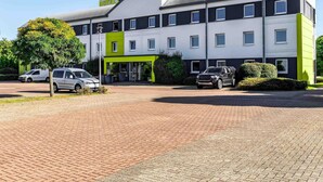 A modern hotel with a two-story structure, a green and white color scheme, and a parking area with cars. - B&B Hotel Braunschweig-Nord (Braunschweig)