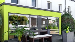 A modern outdoor seating area with wicker furniture and potted plants, adjacent to a building with large glass windows. - B&B Hotel Braunschweig-Nord (Braunschweig)