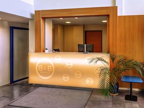 Una recepción con el logo de B&B, una planta pequeña y una silla azul.