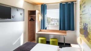A hotel room with a bed, a TV mounted on the wall, a window with curtains, a wooden shelf, and two green stools. - B&B Hotel Braunschweig-Nord (Braunschweig)