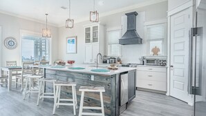 A modern kitchen with a central island, white cabinetry, stainless steel appliances, and a large window providing natural light. - Sea Turtle - Luxury 7BR Beachfront Retreat, Private Pool, 5 Star Reviews! (Panama City Beach)