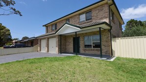 Ein zweistöckiges Backsteinhhaus mit Garage, überdachter Veranda und umzäunter Garten.