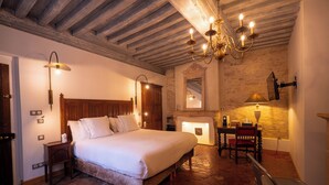 Une chambre à coucher avec un grand lit, un plafond en bois, un lustre, une cheminée et un bureau avec une chaise.