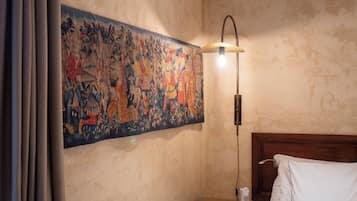 Une chambre d’hôtel avec une grande tapisserie au mur, une table de chevet avec une lampe et un lit recouvert de draps blancs.