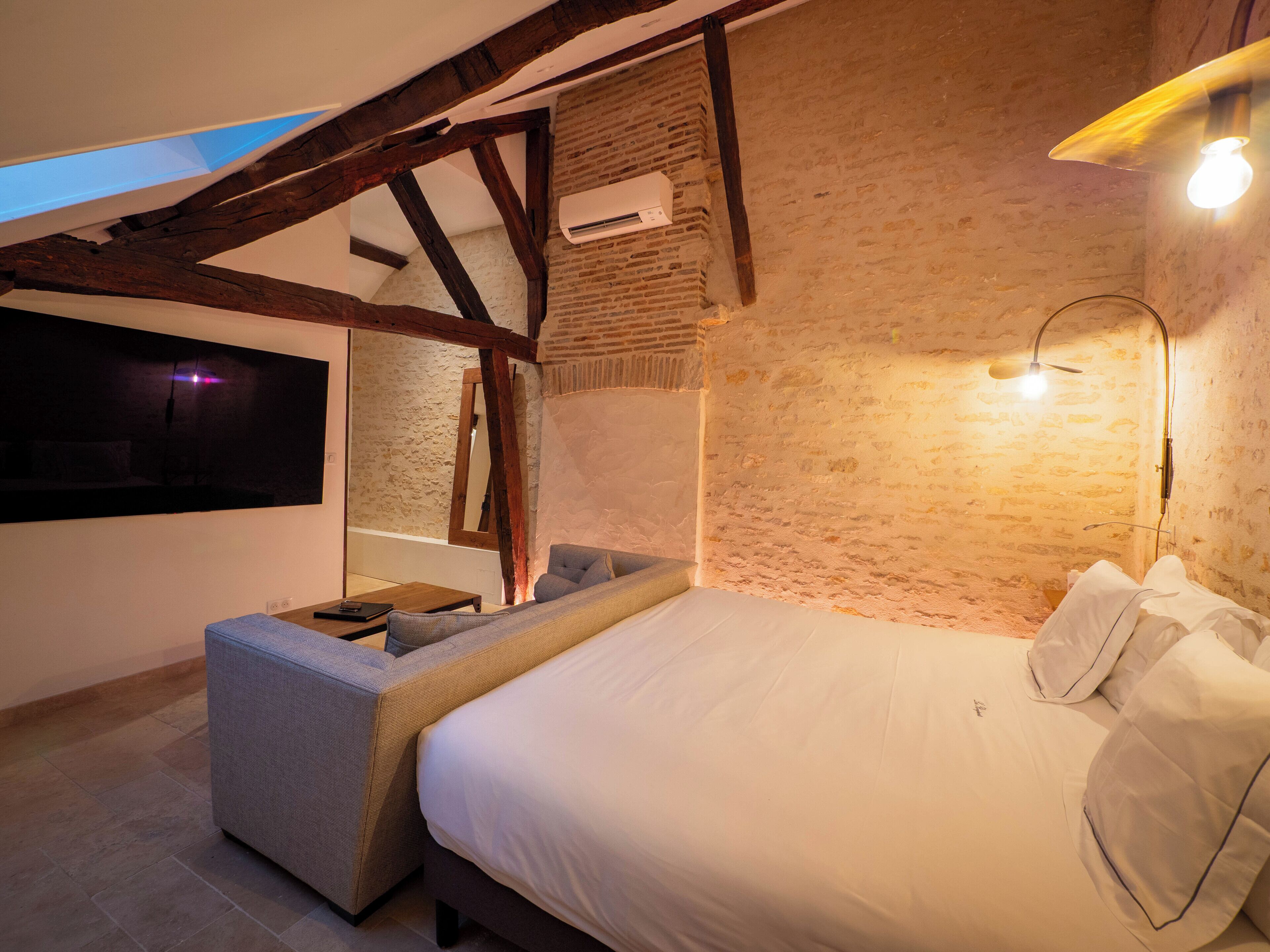 Een slaapkamer met een bed, een bank, een televisie en een bakstenen muur.
