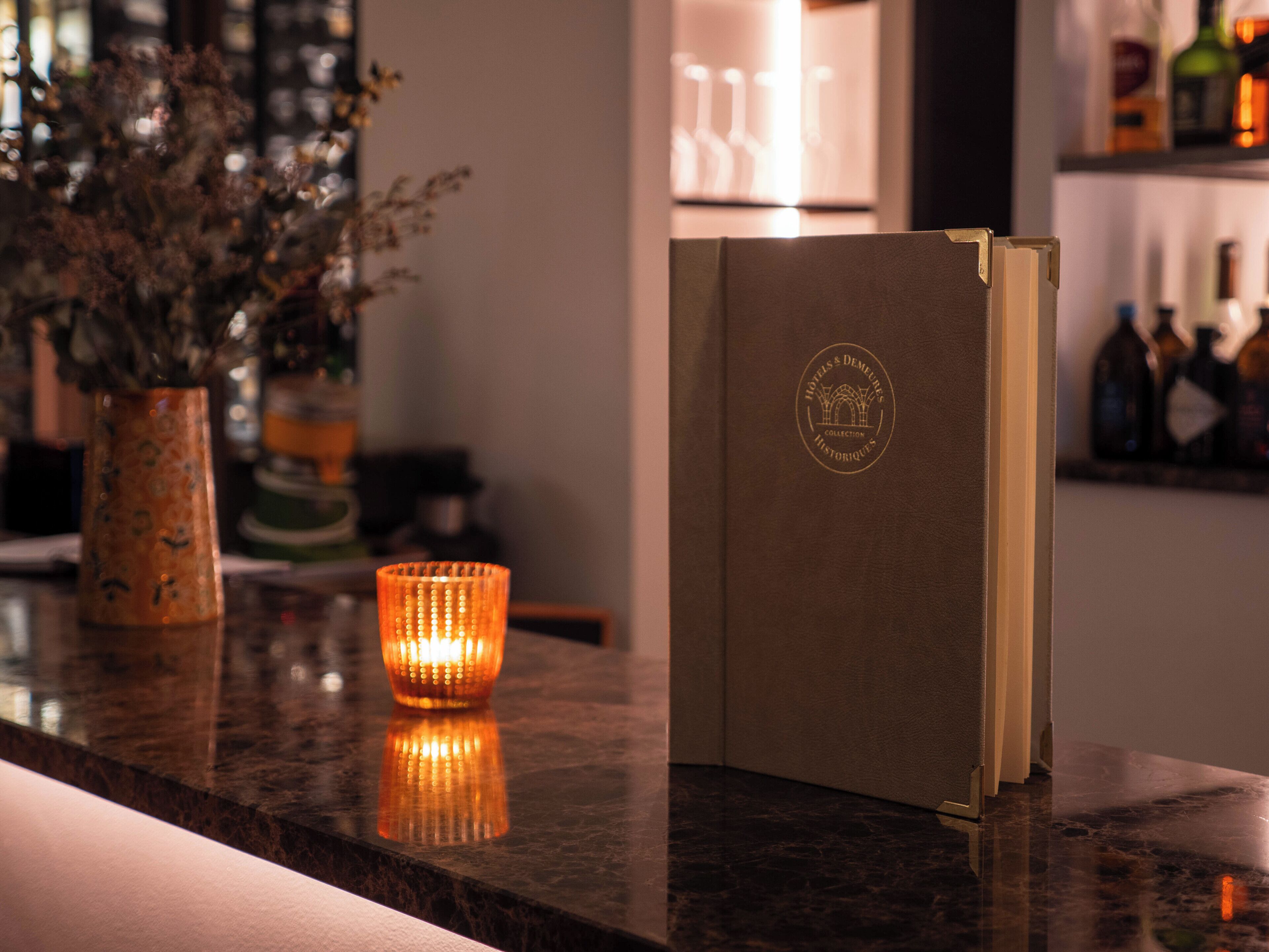 A bar area with a candle, a book, and a vase of dried flowers.