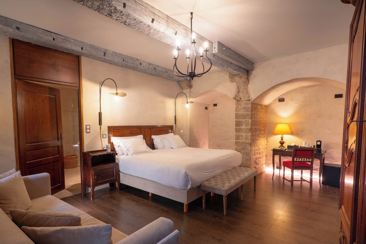 Ein Schlafzimmer mit einem großen Bett, einem Holz-Kopfteil, einer Bank, einem Schreibtisch mit Stuhl und einer Lampe.