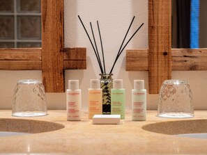 A bathroom counter with various Clarins Paris skincare products, a small vase with reed diffusers, and two empty glass vases. - Les Remparts Hôtels et Demeures Historiques (Beaune)
