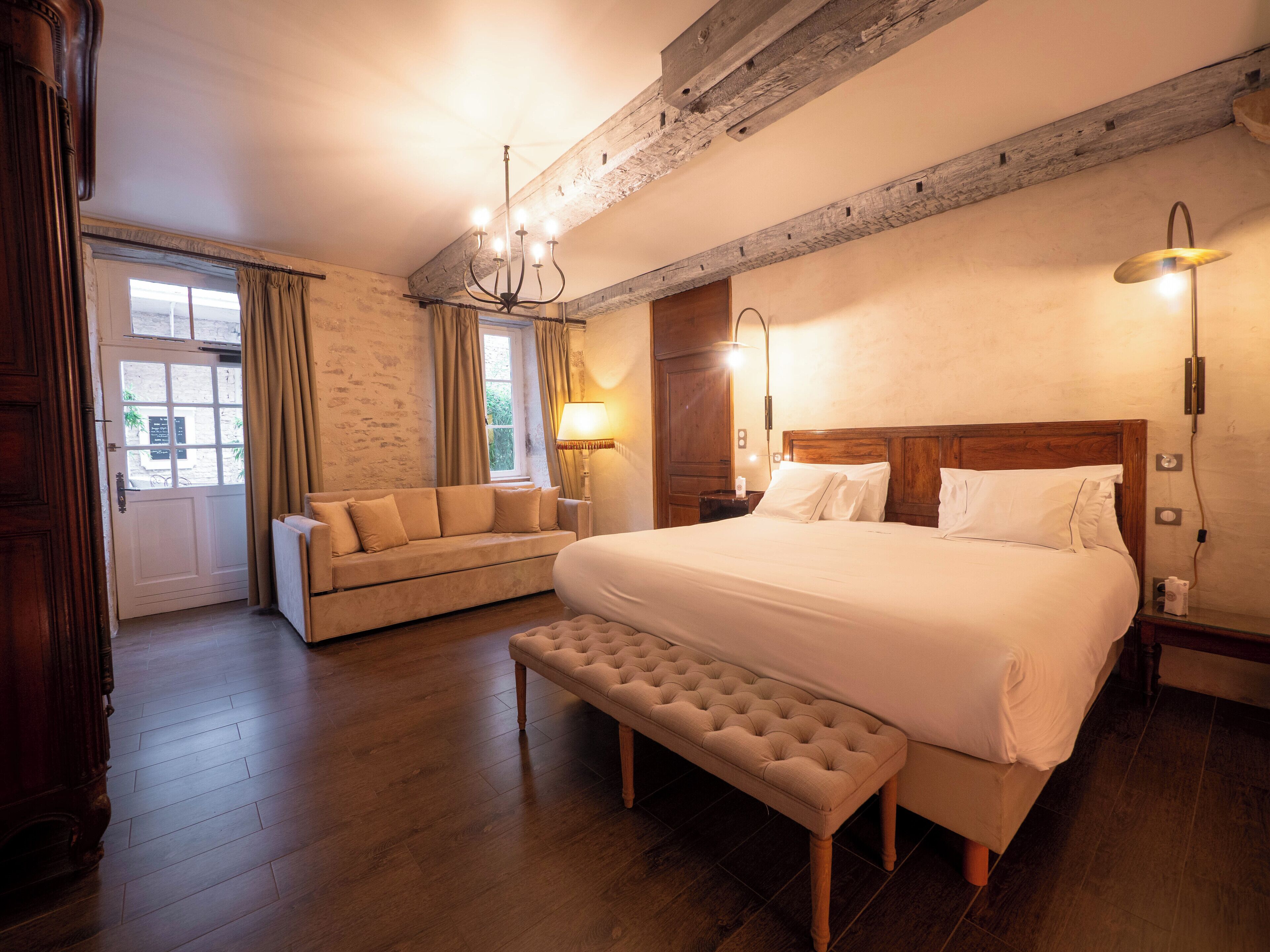 Une chambre spacieuse avec un grand lit, un banc, un canapé et un lustre.