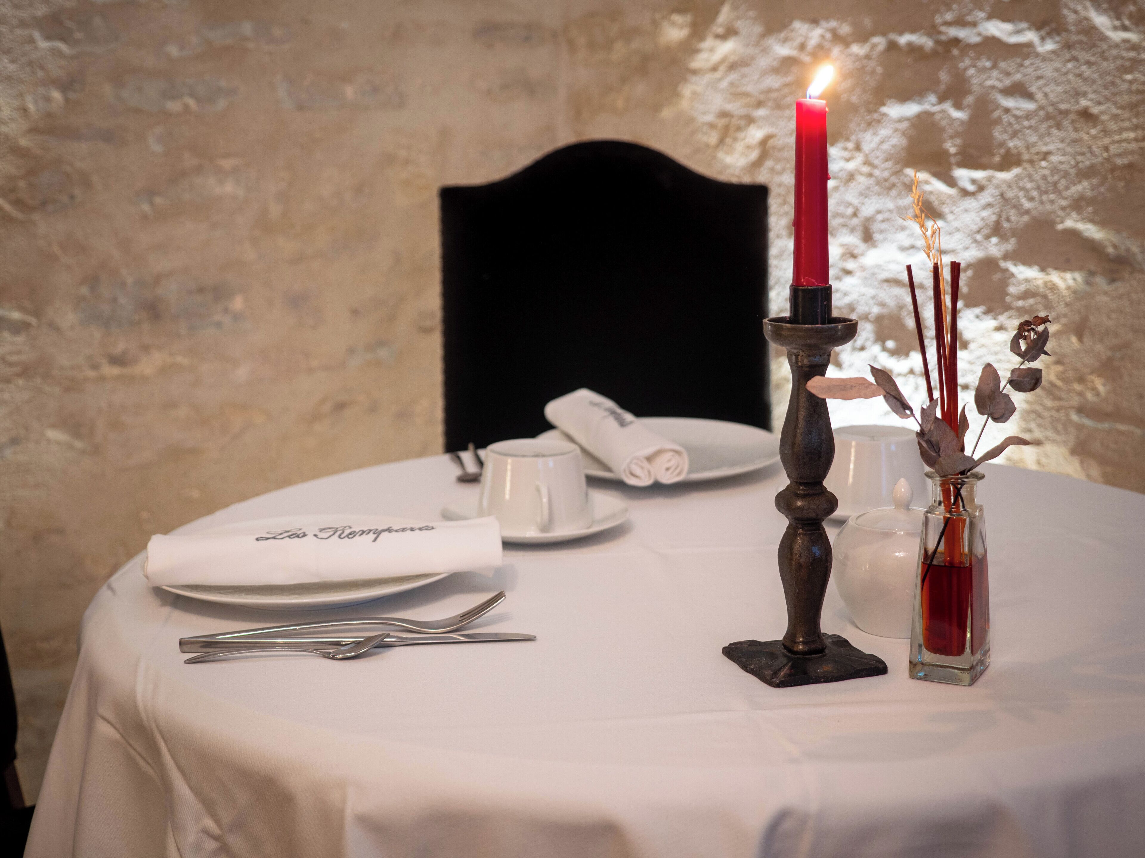A table set with a candle, a glass vase with dried flowers, a folded napkin, a cup, and a plate.