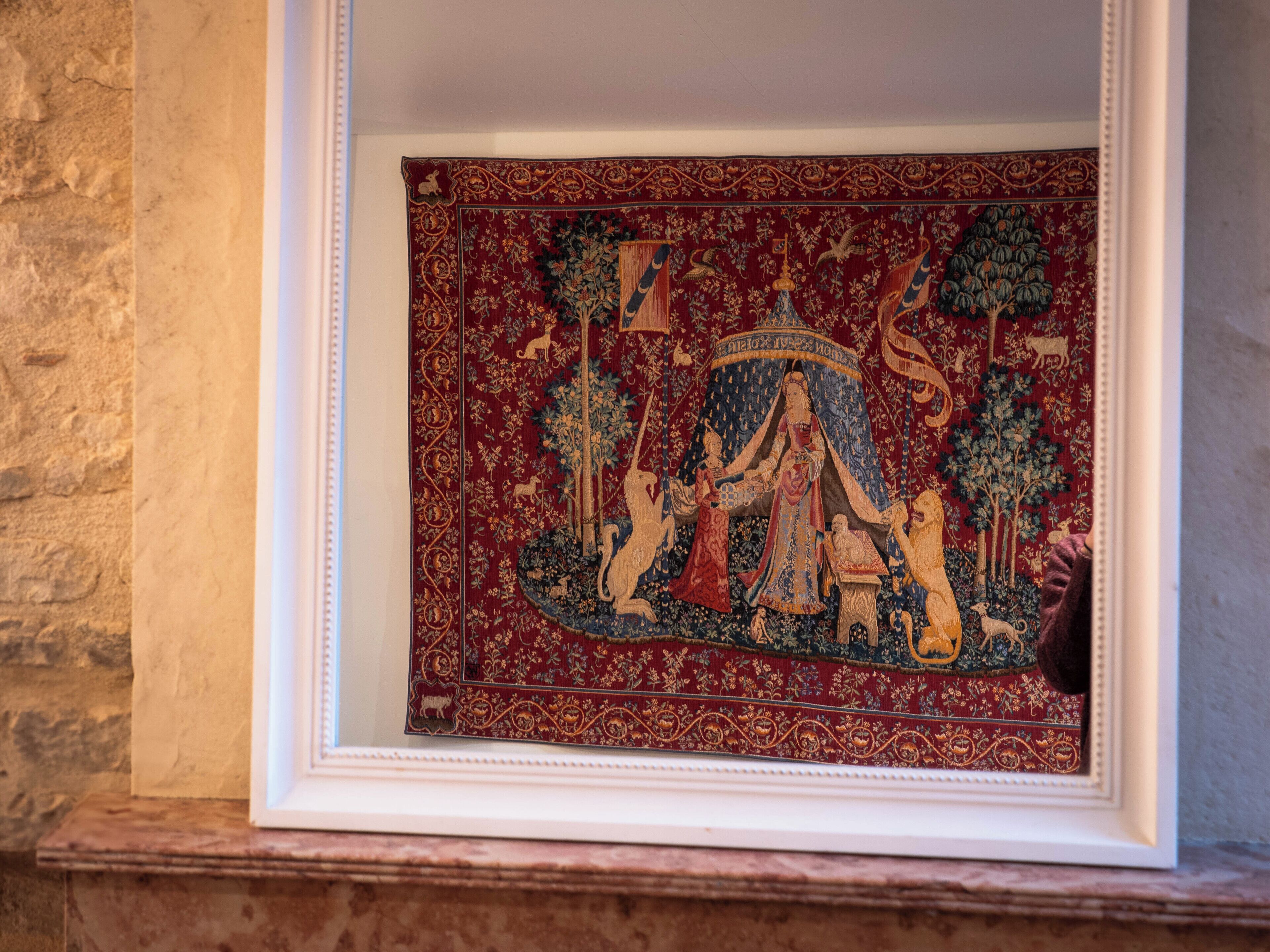 Une tapisserie encadrée, ornée de motifs et de figures complexes, est accrochée à un mur.