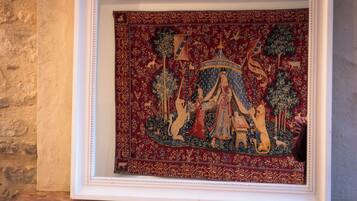 Une tapisserie encadrée, ornée de motifs et de figures complexes, est accrochée à un mur.