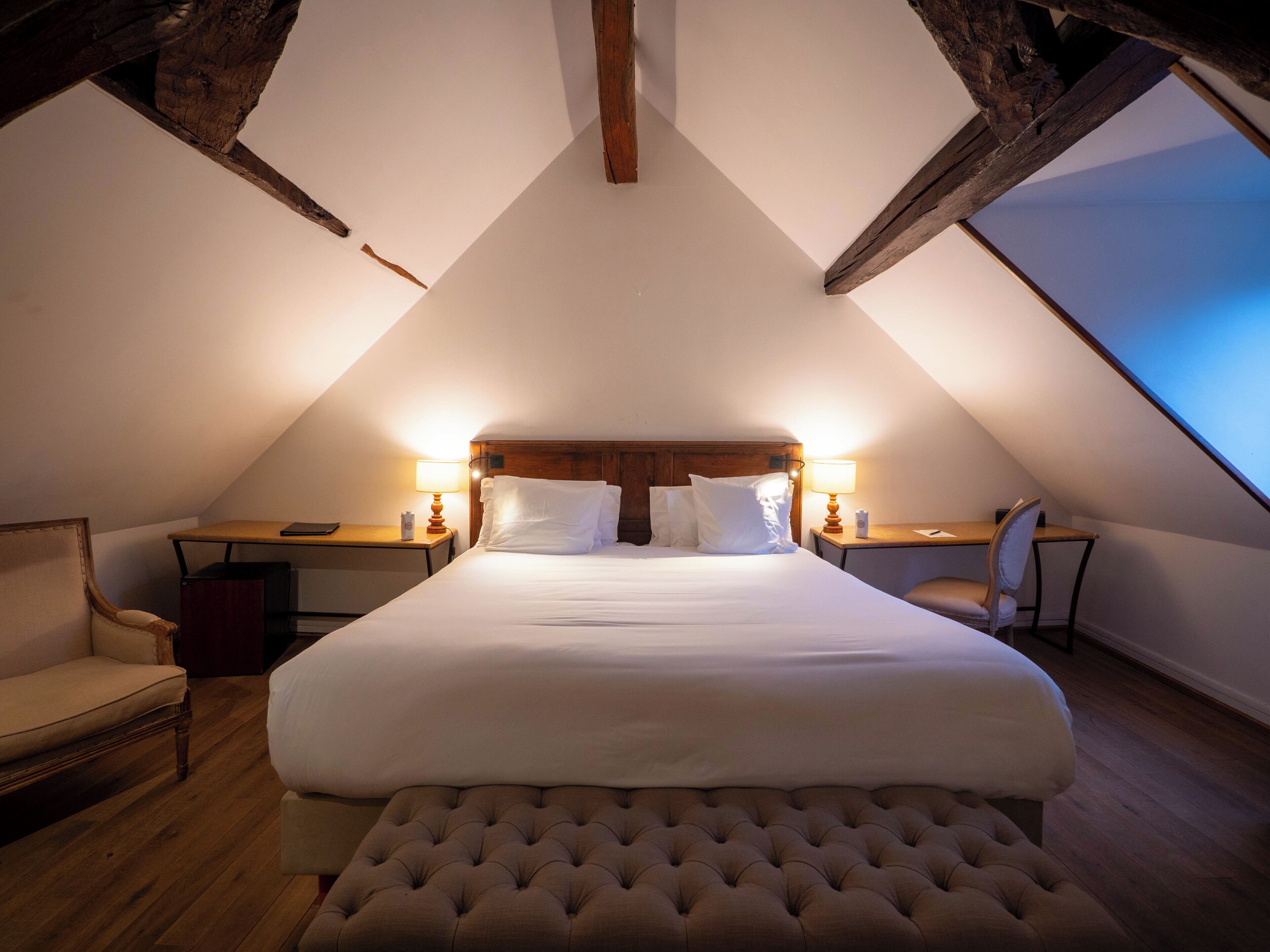 A bedroom with a large bed, two bedside tables, a chair, and a wooden ceiling.