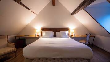A bedroom with a large bed, two bedside tables, a chair, and a wooden ceiling.
