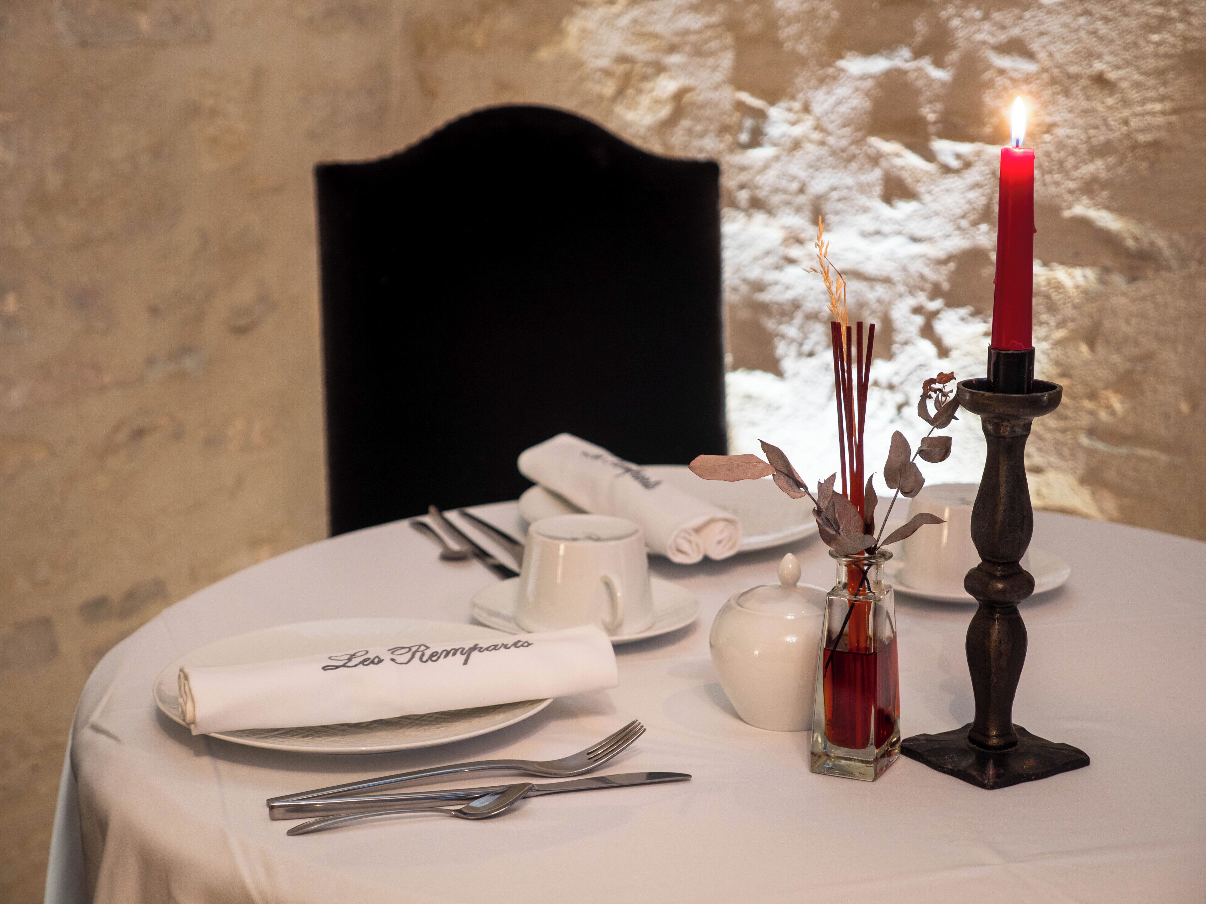 Una mesa con un candelero, un jarrón pequeño con flores secas y una servilleta doblada con texto.