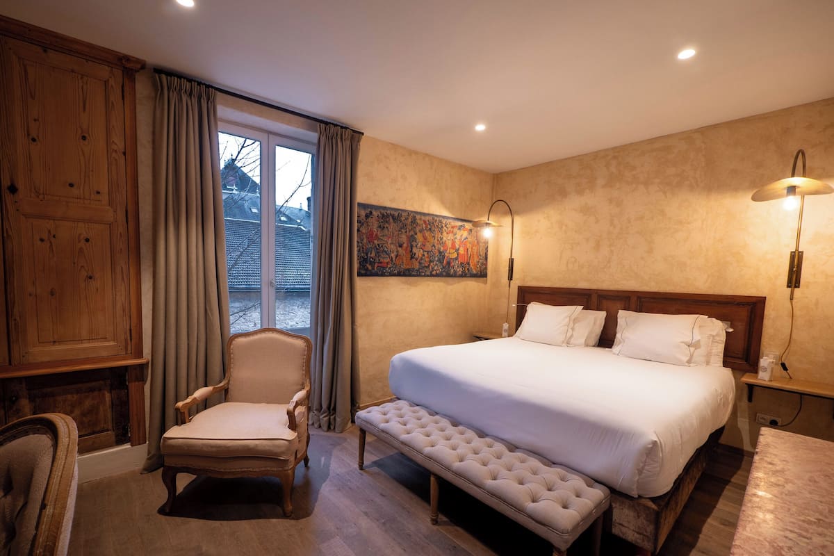 Ein Schlafzimmer mit einem großen Bett, einem Sessel, einer Bank und einem Bild an der Wand.