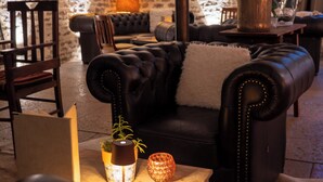 Un salon chaleureux avec un mur en pierre, un canapé en cuir, une table basse en bois et un grand lampadaire.